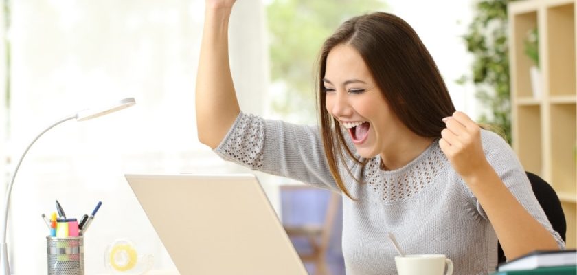 A woman is excited and celebratory in front of her laptop thanks to a successful marketing campaign.
